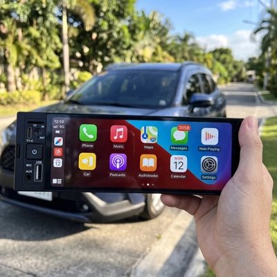 Autoradio CarPlay Serenity tenu en main devant une voiture, écran panoramique allumé